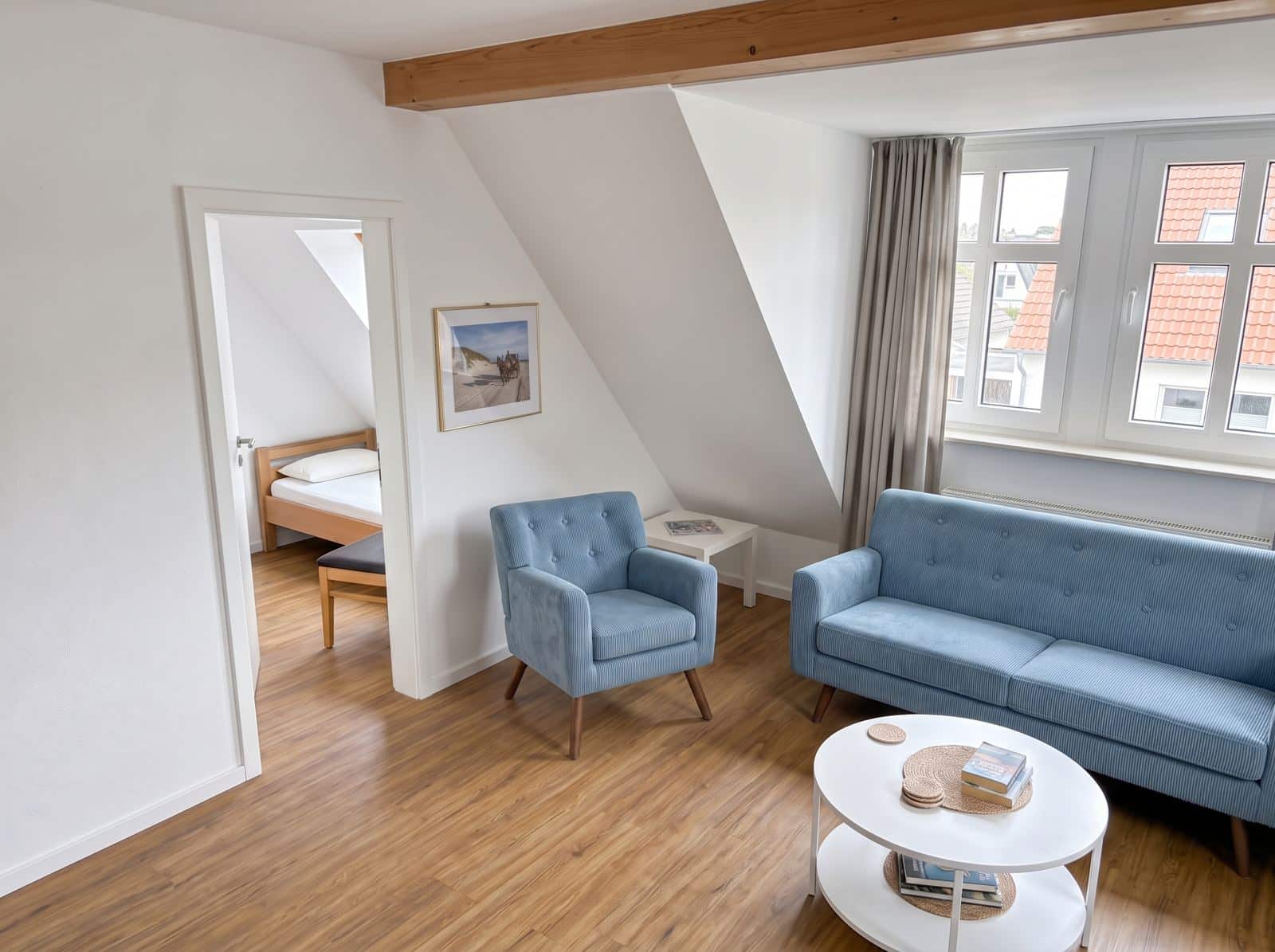 Wohnbereich der Ferienwohnung 301 mit Sofa und Sessel, durch die offene Tür das separate Zimmer